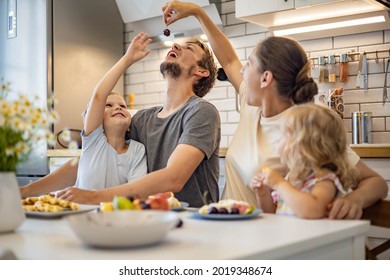 Happy Family Enjoying Weekend Breakfast Together Sitting At Table With Food In Kitchen. Smiling Father, Mother And Kids Relaxing Eating Fresh Homemade Summer Dessert Waffles With Fruits Feeling Love