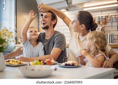 Happy Family Enjoying Weekend Breakfast Together Sitting At Table With Food In Kitchen. Smiling Father, Mother And Kids Relaxing Eating Fresh Homemade Summer Dessert Waffles With Fruits Feeling Love