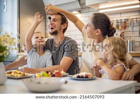 Happy family enjoying weekend breakfast together sitting at table with food in kitchen. Smiling father, mother and kids relaxing eating fresh homemade summer dessert waffles with fruits feeling love