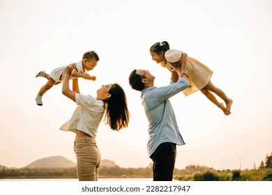 A happy family enjoys a playful moment in a summer field, as the dad and mom throw their child up into the blue sky. The cheerful family looks on with joy and love, Family day - Powered by Shutterstock