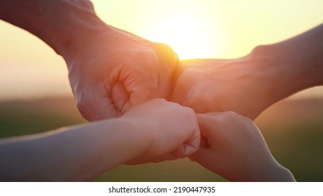 Happy Family Enjoys Successful Life At Back Sunset. Members Give Fists Walking On Evening Meadow. Parents Have Business And Can Ensure Children Life Closeup