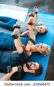 Happy Family Exercising With Dumbbells At Fitness Studio