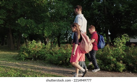 Happy Family. Father Leads Children By Hand School. Boy Girl Child With School Backpacks Rush Lesson. Caring Dad With His Daughter Son Are Walking Around School Yard. Happy Family Concept. Teamwork