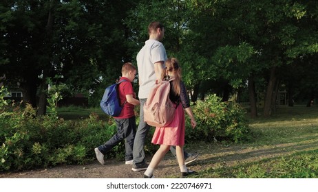 Happy Family. Father Leads Children By Hand School. Boy Girl Child With School Backpacks Rush Lesson. Caring Dad With His Daughter Son Are Walking Around School Yard. Happy Family Concept. Teamwork