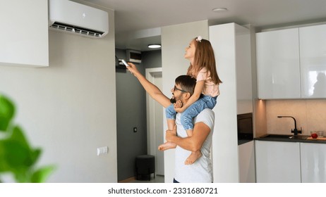Happy family, father with little daughter on shoulders turn on air conditioner using remote control. - Shutterstock ID 2331680721