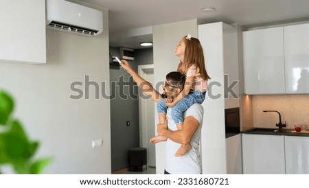 Happy family, father with little daughter on shoulders turn on air conditioner using remote control.