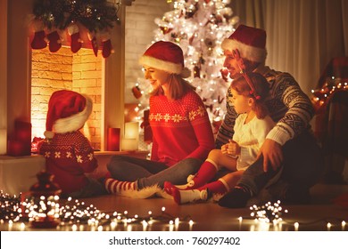 Happy Family Father Mother And Children Sitting By Fireplace On Christmas Eve
