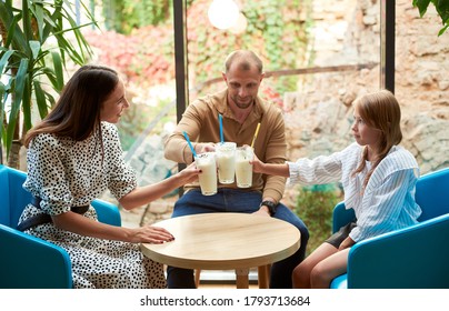 Happy Family - Father, Mother And Daughter Having Drinks, Clinking Glasses With Milkshakes. Focus Is On Milkshakes. Concept Of Restaurant, Drinks And Hospitality.