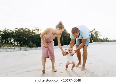 Happy Family Of Father, Mother And Little Baby Boy Together On Sandy Beach On Sunset