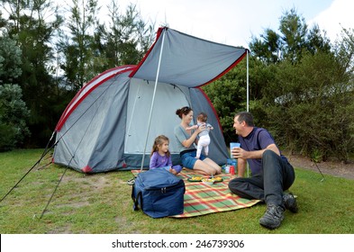 Happy Family, Father And Mother With One  Small Girl And A Baby, Camping Together In A Tent In Outdoors Camp Site In The Nature. Real People. Copy Space