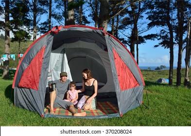 Happy family, father and mother with one child (girl age 5), camping together in a large tent in an outdoors camp site in the North Island of New Zealand.