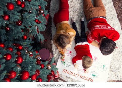 Happy Family: Father, Mother And Son Writing Future Resolutions And Plans Of Family In Coming 2019 New Year Before Night Of Christmas Eve And Happy New Year Near Decorated Green Christmas Tree.