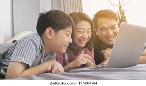 Happy family Father mother and son watching on laptop computer and having fun, Asian family rest on bed with laptop computer - Powered by Shutterstock