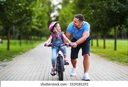 Happy Family Father Teaches Child Daughter To Ride A Bike In The Park In Nature
