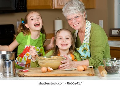 Happy Family Featuring A Friendly Grandma Baking Cookies In A Home Kitchen With Her Two Grandchildren.