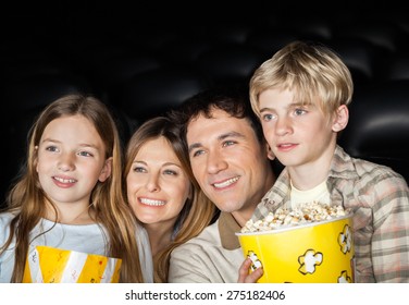 Happy Family Of Four Holding Popcorn While Watching Film In Movie Theater