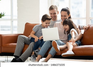 Happy family of four parents and cute little kids children enjoy using laptop watching cartoons, make internet video call or shopping online looking at computer screen sit together on sofa at home