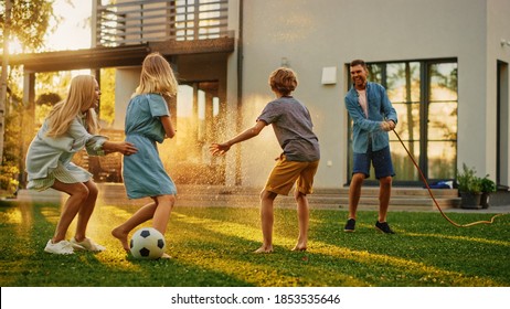 Happy Family Of Four Playing With Garden Water Hose, Spraying Each Other. Mother, Father, Daughter And Son Have Fun Playing Games In The Backyard Lawn Of Idyllic Suburban House On Sunny Summer Day