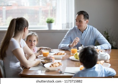 Happy Family Of Four Sit At Table Enjoy Tasty Healthy Breakfast Together, Mom Dad And Two Kids Have Delicious Morning Food In Kitchen Talking, Children With Parents Eat Oatmeal And Croissants At Home