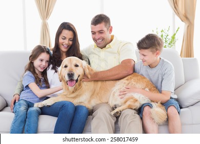 Happy Family Of Four Stroking Golden Retriever In Living Room