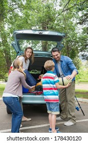 Happy Family Of Four Unloading Car Trunk While On Picnic