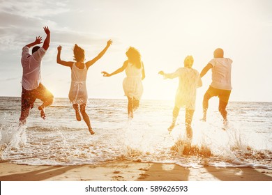 Happy family or friends at the beach running and jumping in the sunset sea. Friendship or vacations concept - Powered by Shutterstock