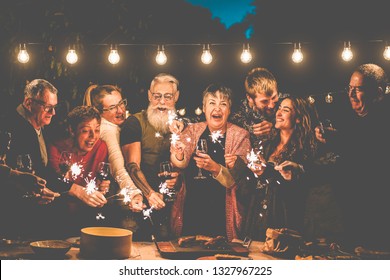 Happy family and friends celebrating with sparkler fireworks after dinner - Different age of people having fun drinking wine at birthday bbq party outdoor - Celebration concept - Focus on center faces