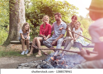 Happy family and friends roasting sausages over burning campfire at park