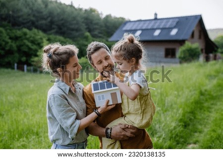 Happy family in front of their house with solar panels on the roof.