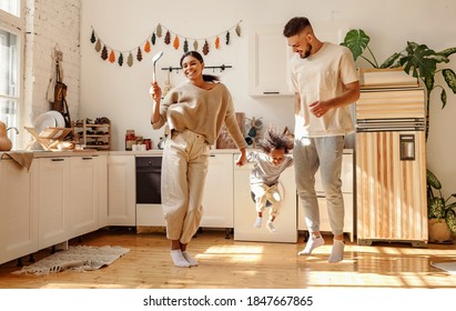 Happy Family: Full Body Delighted Diverse Parents Playing And Dancing With Son In Cozy Kitchen On Weekend Day At Home
