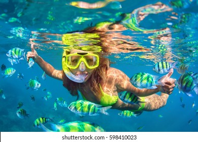 Happy family - girl in snorkeling mask dive underwater with fishes school in coral reef sea pool. Travel lifestyle, water sport outdoor adventure, swimming lessons on summer beach holidays with child.