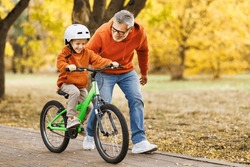 Happy Family Grandfather Teaches Boy Grandson  To Ride A Bike In Autumn Park   In Nature