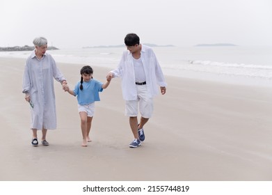 Happy Family Grandmother And Grandfather Holding Hand And Walk With Grandchild On The Beach	