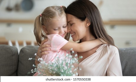 Happy Family Grateful Attractive Young Mum Holding Spring Flowers Embracing Sweet Adorable Little Child Daughter At Home, Cute Small Kid Girl Hugging Mom Presenting Bouquet On Mothers Day Concept