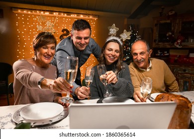 Happy family greeting their family and friends with a champagne glass, on New Year's eve using a skype video call. Relatives looking to a laptop. Social distancing during the coronavirus pandemic.