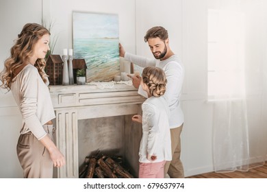 Happy Family Hanging Picture Of Sea Over The Fireplace At Home