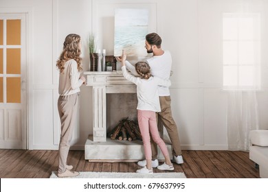 Happy Family Hanging Picture Of Sea Over The Fireplace At Home