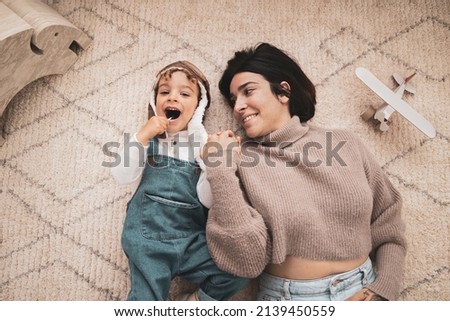 Happy family have fun at home. Mother and her son playing together. Boy dressed as a pilot while his mother holds his hand. Aerial view
