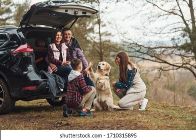 Família feliz se diverte com seu cachorro perto de um carro moderno ao ar livre na floresta.
