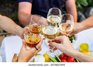 Happy family having dinner at the summer garden party and clinking drinks. People say toast and drink. Festive family dinner in the backyard. Male and female hands holding glasses of wine. Lifestyle