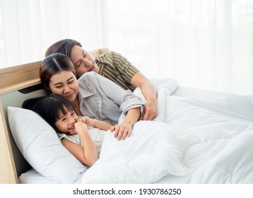 happy family having fun in bed room concept. father,mother and daugther smiling face, kiss love together lying on bed with duvet cover them copy space.