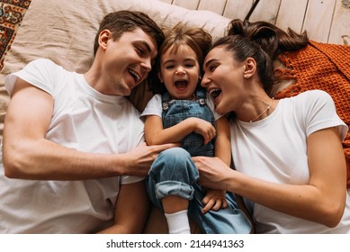 Happy family having fun in the bedroom while they lie on bed. Happy young family. Happy family laying on bed in bedroom with happy and smile, top view. Family relationships concept. Stock photo - Powered by Shutterstock