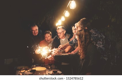 Happy Family Having Fun At Dinner Night Party Outdoor - Group Of People Mixed Ages Celebrating Together With Fireworks Sparklers Outside - Holidays Culture And Parenthood Lifestyle Concept