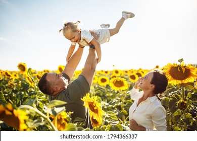 Happy Family Having Fun In The Field Of Sunflowers. Father And Mother Throw Their Daughter In The Air And Smile. Girl Likes Playing With Her Parents. Summer Season, Freedom, Family Value Concept.