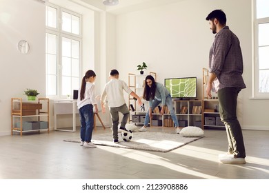 Happy family having fun at home. Kids playing soccer with mom and dad. Brother and sister playing football together with parents in big living room with large television set in new modern apartment