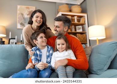 Happy family having fun at home, parents and little children sit on sofa together, Happy family sitting on sofa laughing together. Cheerful parents playing with their kids at home. - Powered by Shutterstock