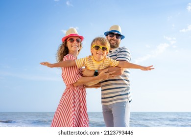 Happy family having fun on the beach. Mother and father holding son against blue sea and sky background. Summer vacation concept - Shutterstock ID 2123793446