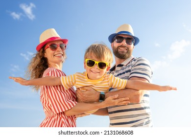 Happy Family Having Fun On The Beach. Mother And Father Holding Son Against Blue Sea And Sky Background. Summer Vacation Concept