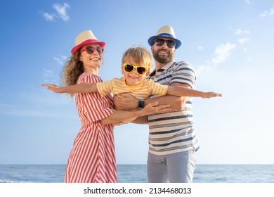 Happy family having fun on the beach. Mother and father holding son against blue sea and sky background. Summer vacation concept - Shutterstock ID 2134468013