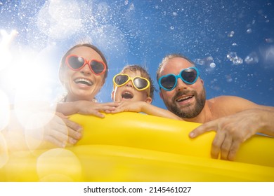 Happy Family Having Fun On Summer Vacation. People Jumping In Swimming Pool Against Blue Sky Background. Active Holiday Concept. Spring Break!